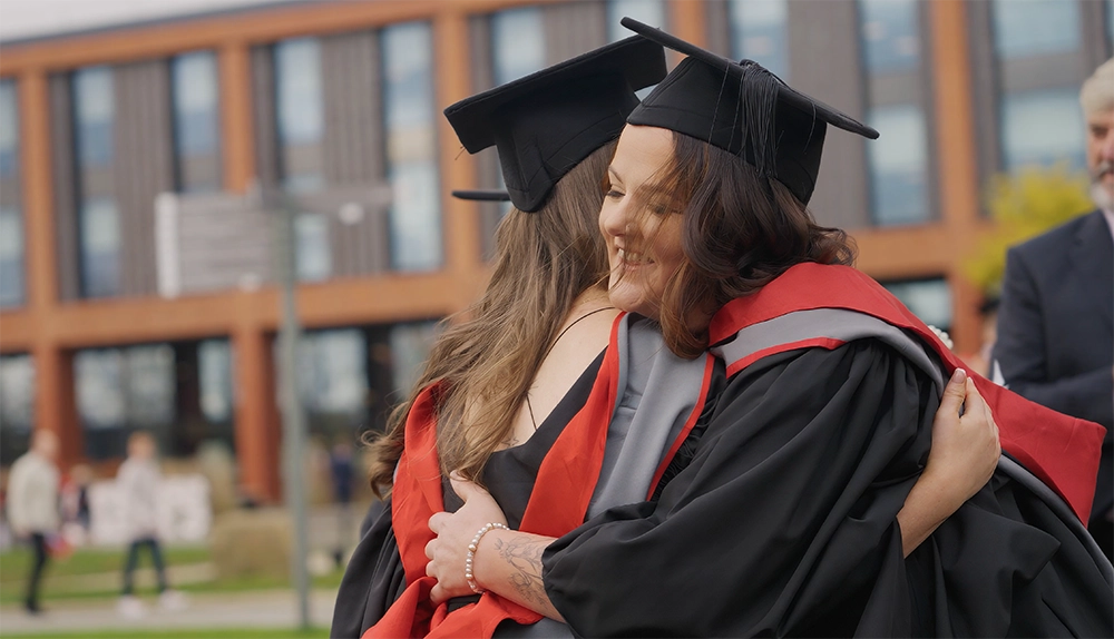 Image of two graduates hugging at graduation.